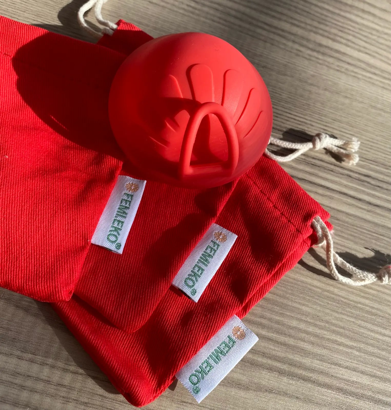 Disc menstrual roșu Femi.Eko® așezat pe săculeți din bumbac roșu personalizați, pe o suprafață din lemn.