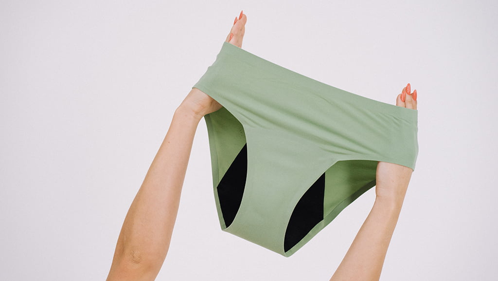 Chilot menstrual verde ridicat de două mâini, evidențiind elasticitatea, materialul moale și designul funcțional pentru protecție și confort.