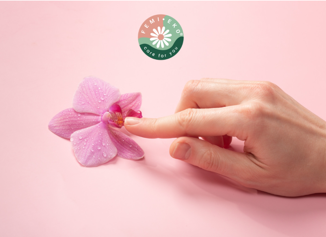 Deget atinge o floare de orhidee roz pe fundal roz, simbolizând delicatețea și intimitatea, logo Femi.Eko® deasupra.