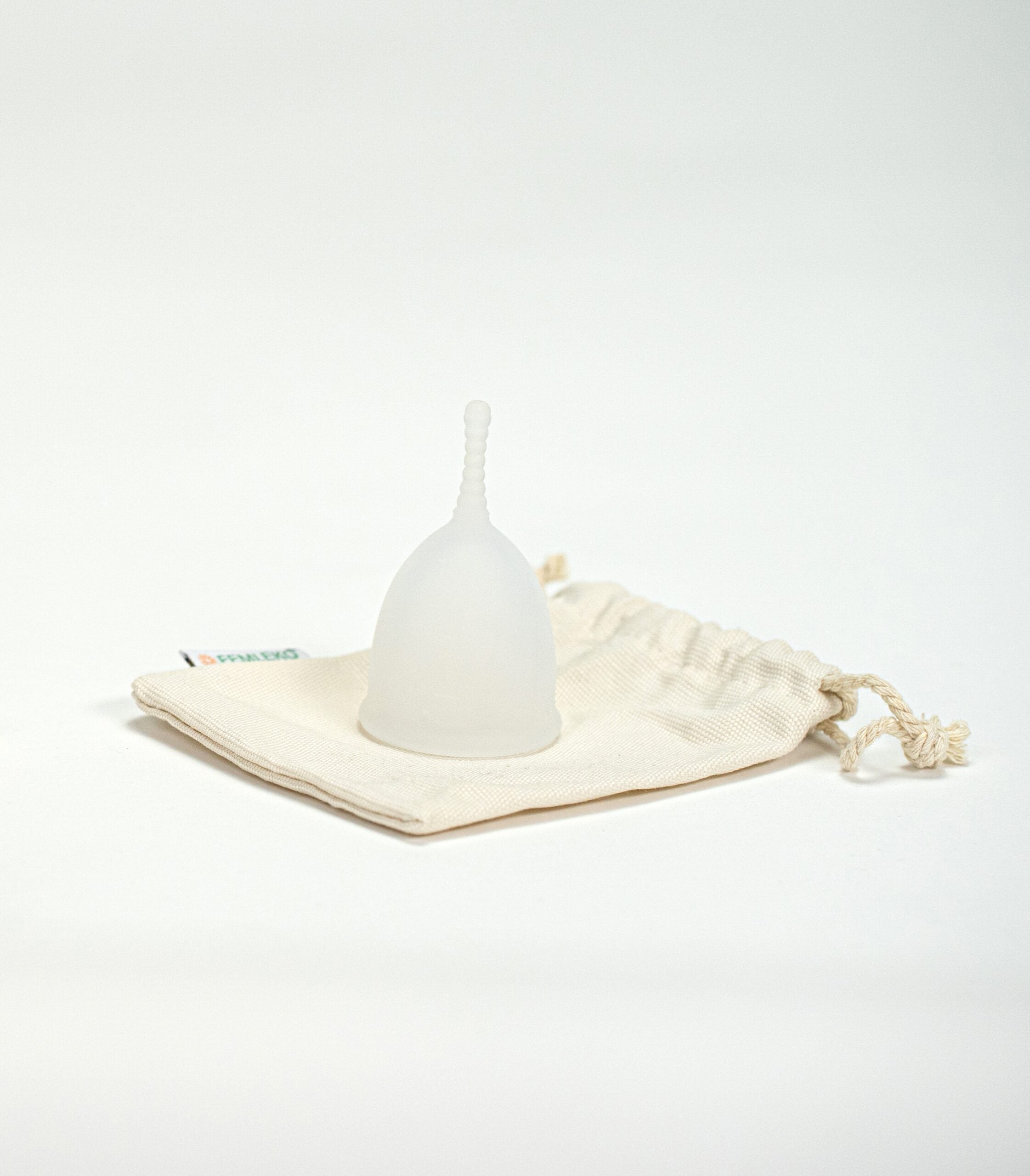 Cupa menstruală Femi.Eko® alb-translucidă, așezată pe un săculeț textil reutilizabil din bumbac, într-un cadru minimalist pe fundal alb.