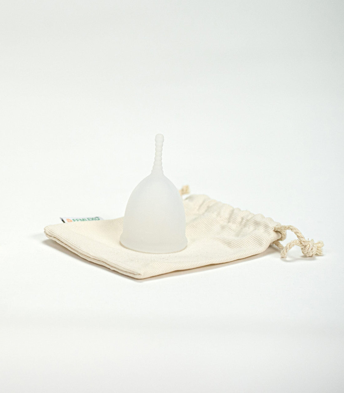 Cupa menstruală Femi.Eko® alb-translucidă, așezată pe un săculeț textil reutilizabil din bumbac, într-un cadru minimalist pe fundal alb.