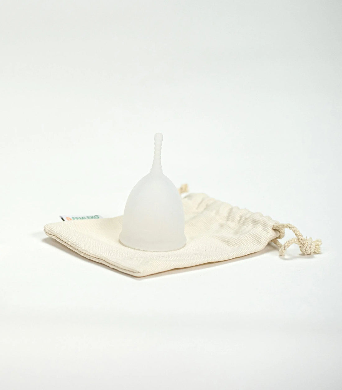 Cupa menstruală Femi.Eko® alb-translucidă, așezată pe un săculeț textil reutilizabil din bumbac, într-un cadru minimalist pe fundal alb.