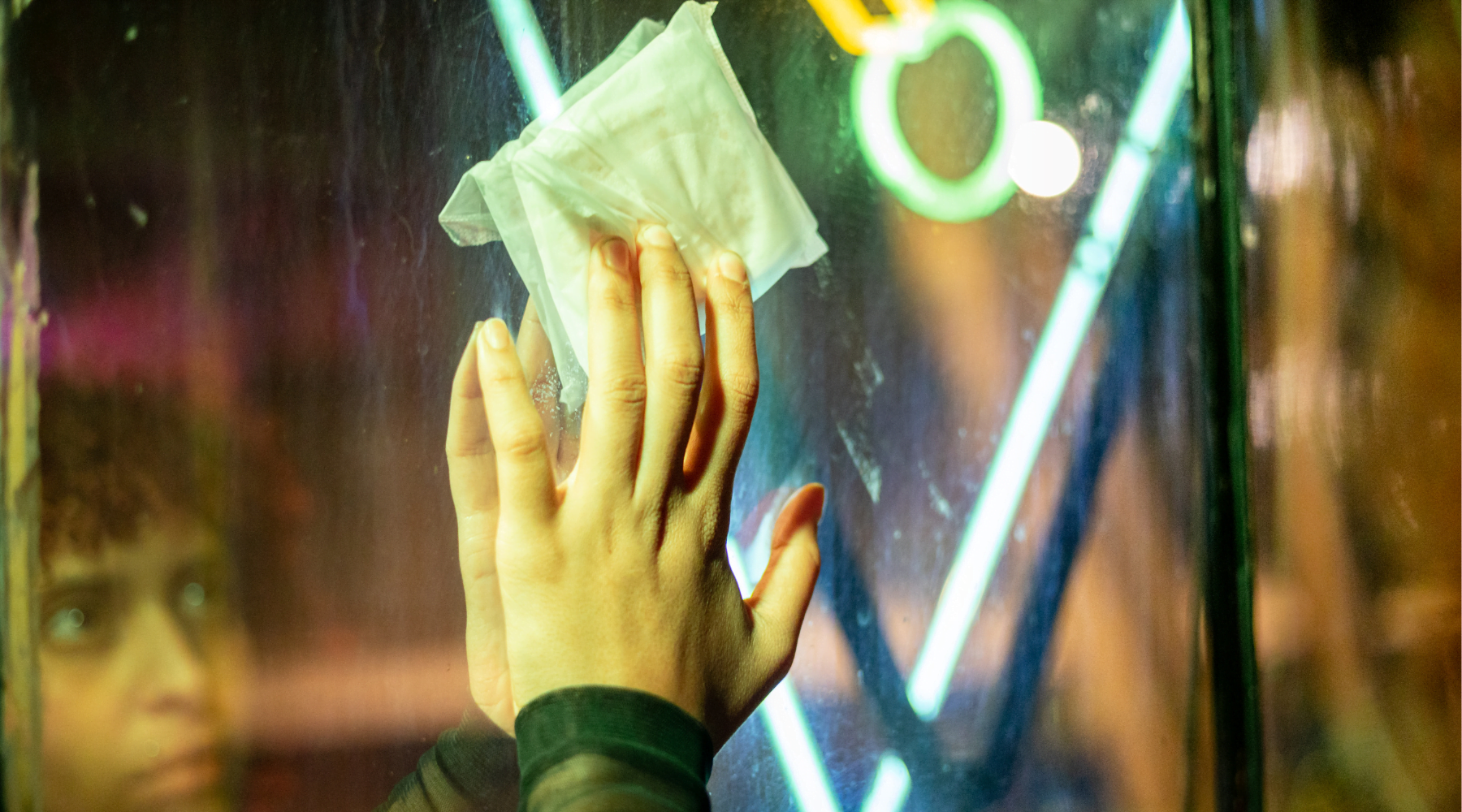 Femeie în oglindă, privind un absorbant prins pe geam – mesaj vizual despre vizibilitate și demnitate menstruală.