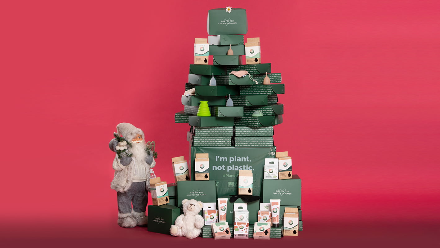 Brad de Crăciun realizat din cutii Femi.Eko® și produse intime reutilizabile, alături de Moș Crăciun și ursuleț de pluș, pe fundal roșu – mesaj ecologic: I'm plant, not plastic.