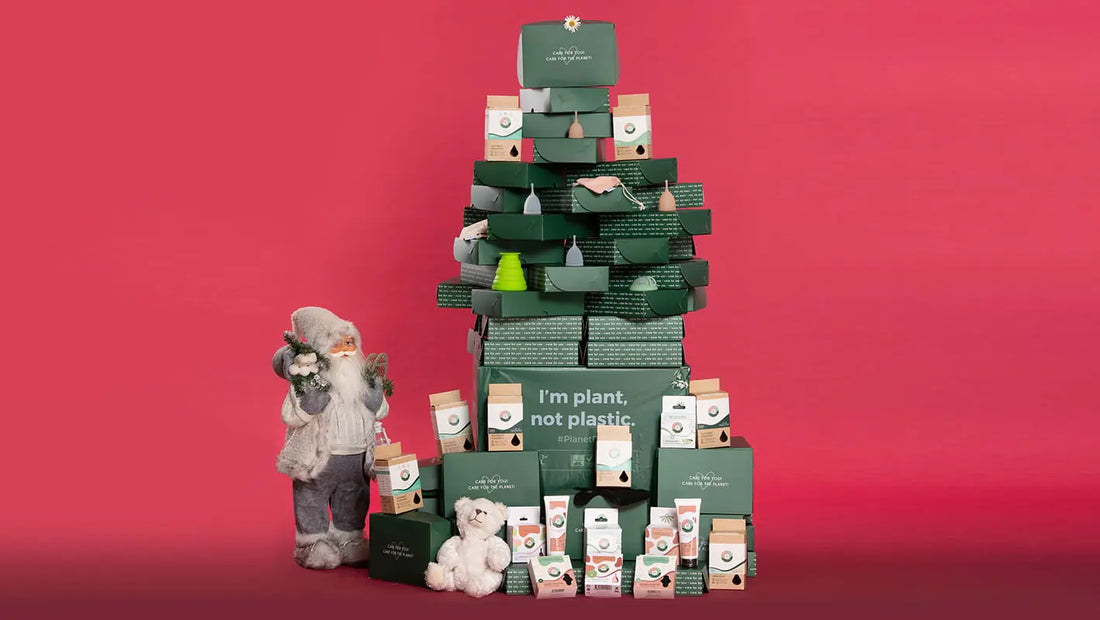 Brad de Crăciun realizat din cutii Femi.Eko® și produse intime reutilizabile, alături de Moș Crăciun și ursuleț de pluș, pe fundal roșu – mesaj ecologic: I'm plant, not plastic.