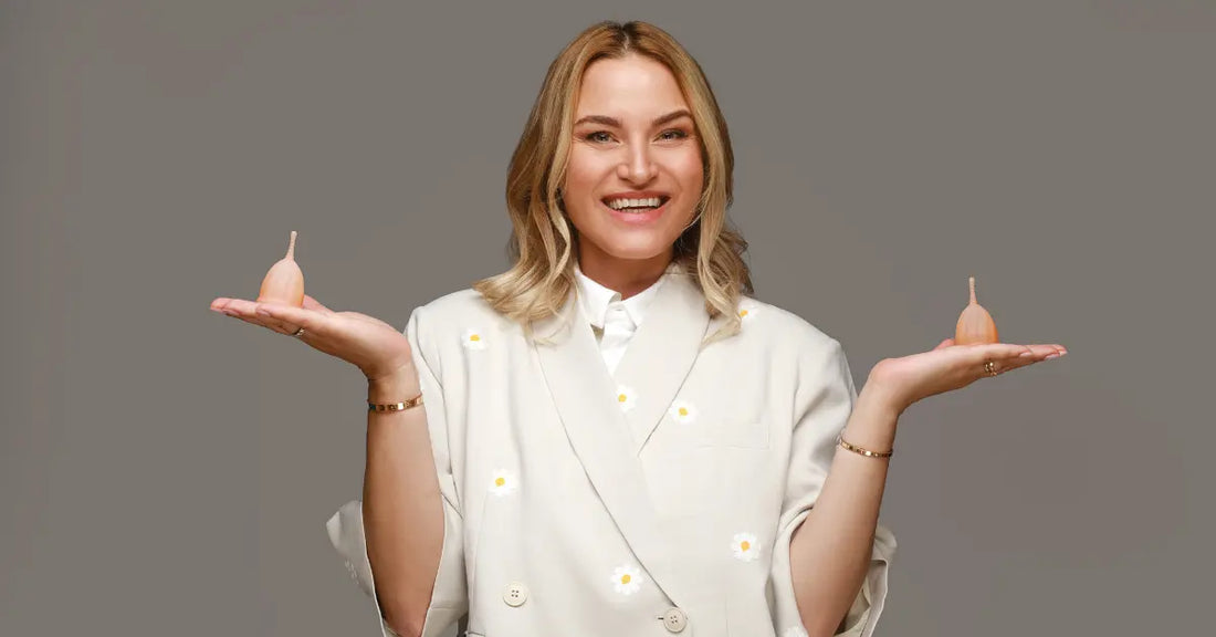 Femeie zâmbitoare ținând două cupe menstruale Femi.Eko® în palme, pe fundal gri.