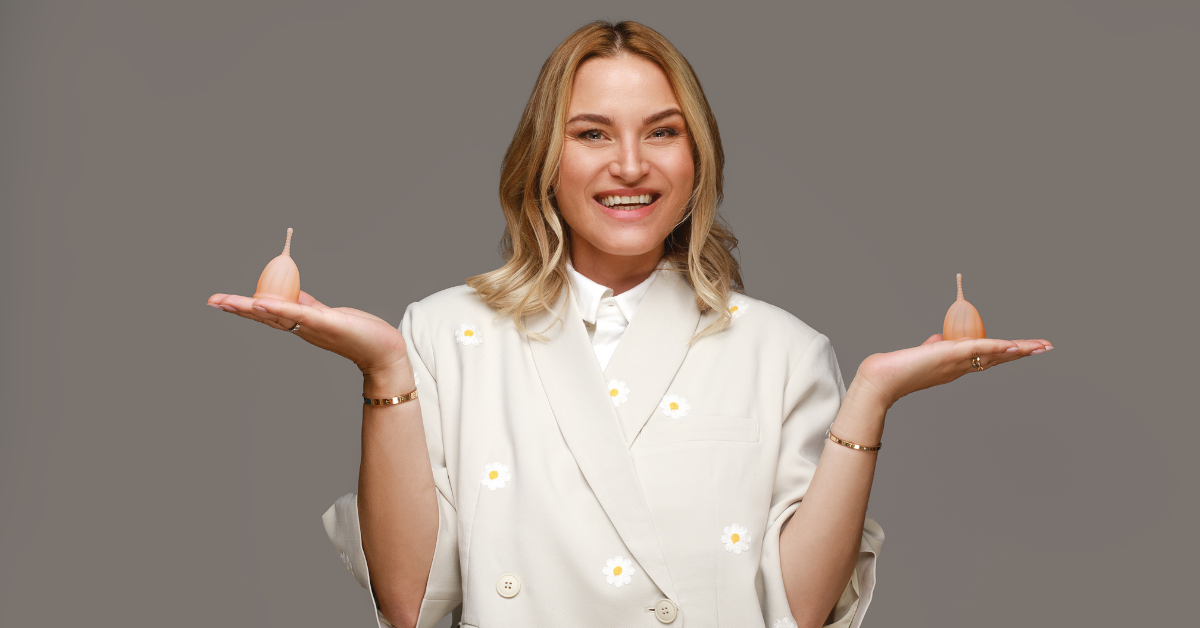 Femeie zâmbitoare ținând două cupe menstruale Femi.Eko® în palme, pe fundal gri.