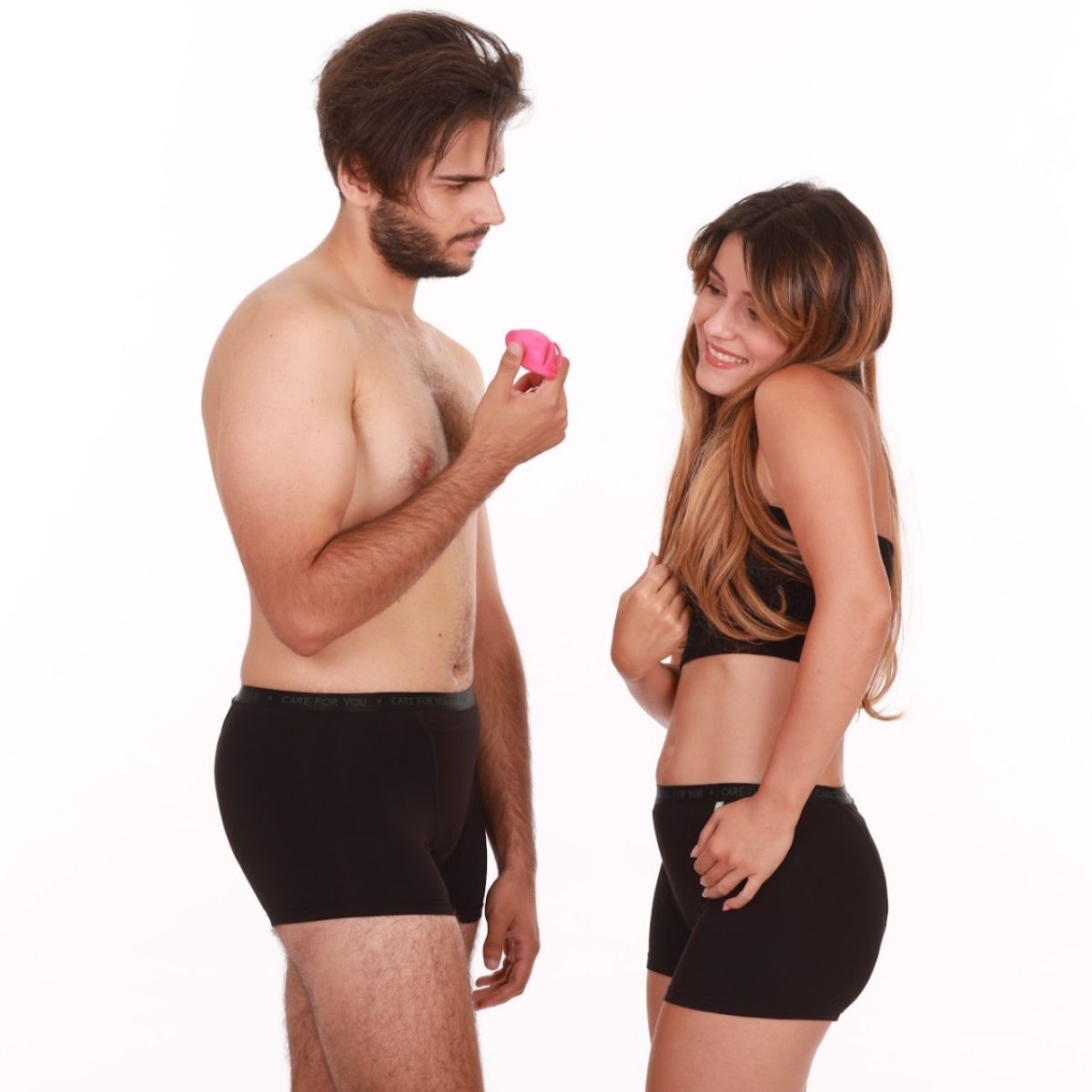 Cuplu îmbrăcat în lenjerie neagră Femi.Eko® ținând un disc menstrual roz și zâmbind jucăuș.