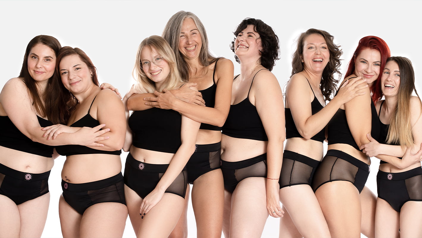 Grup de femei de vârste și forme diferite, purtând lenjerie menstruală neagră Femi.Eko®, zâmbind și îmbrățișându-se – un simbol al diversității, susținerii și confortului în timpul menstruației.